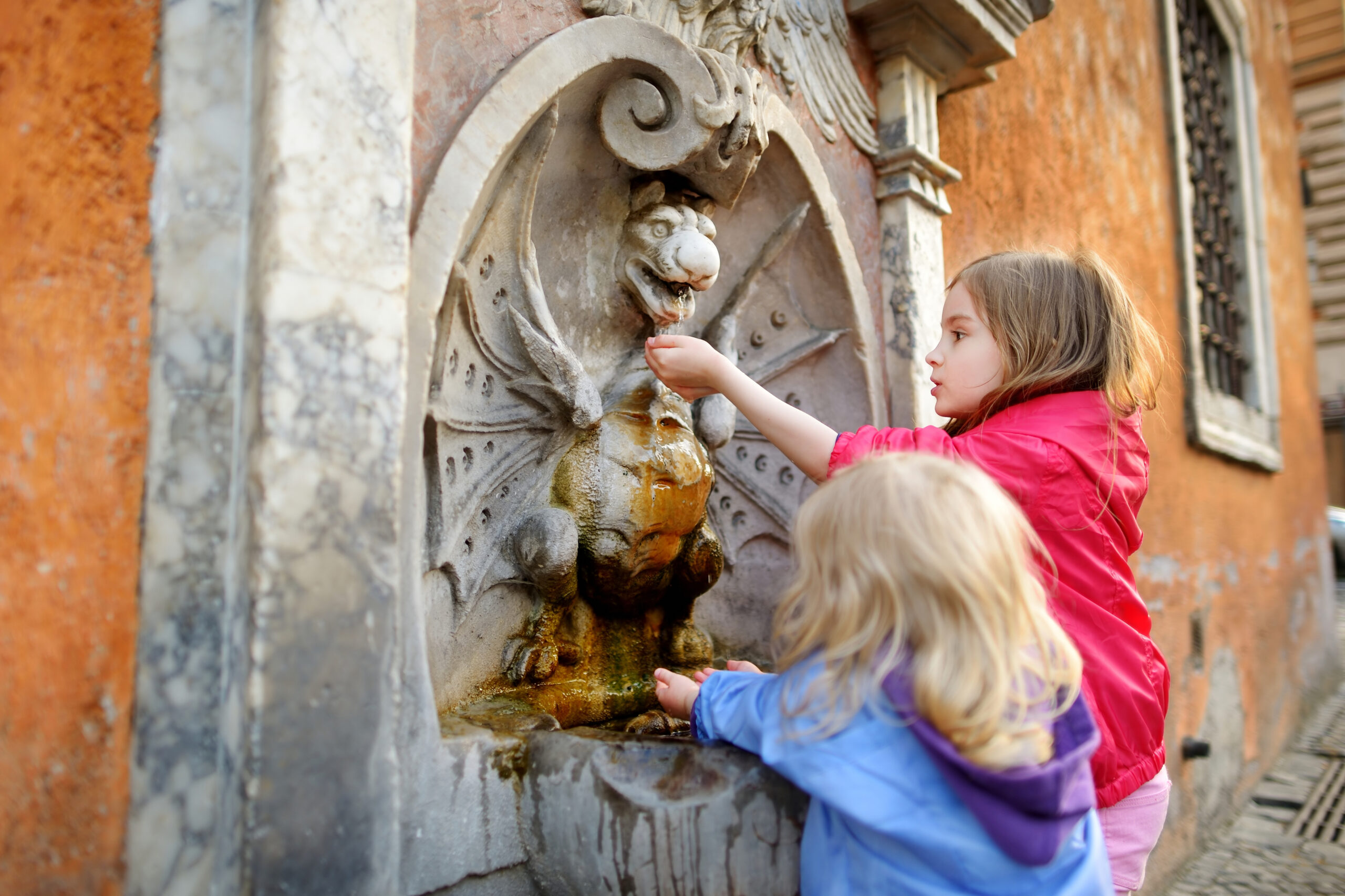 Two,Sisters,Having,Fun,With,Drinking,Water,Fountain,In,Italy